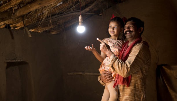 Rural Indian father with daughter delighted at the glow of light bulb and electricity reaching their home after long wait